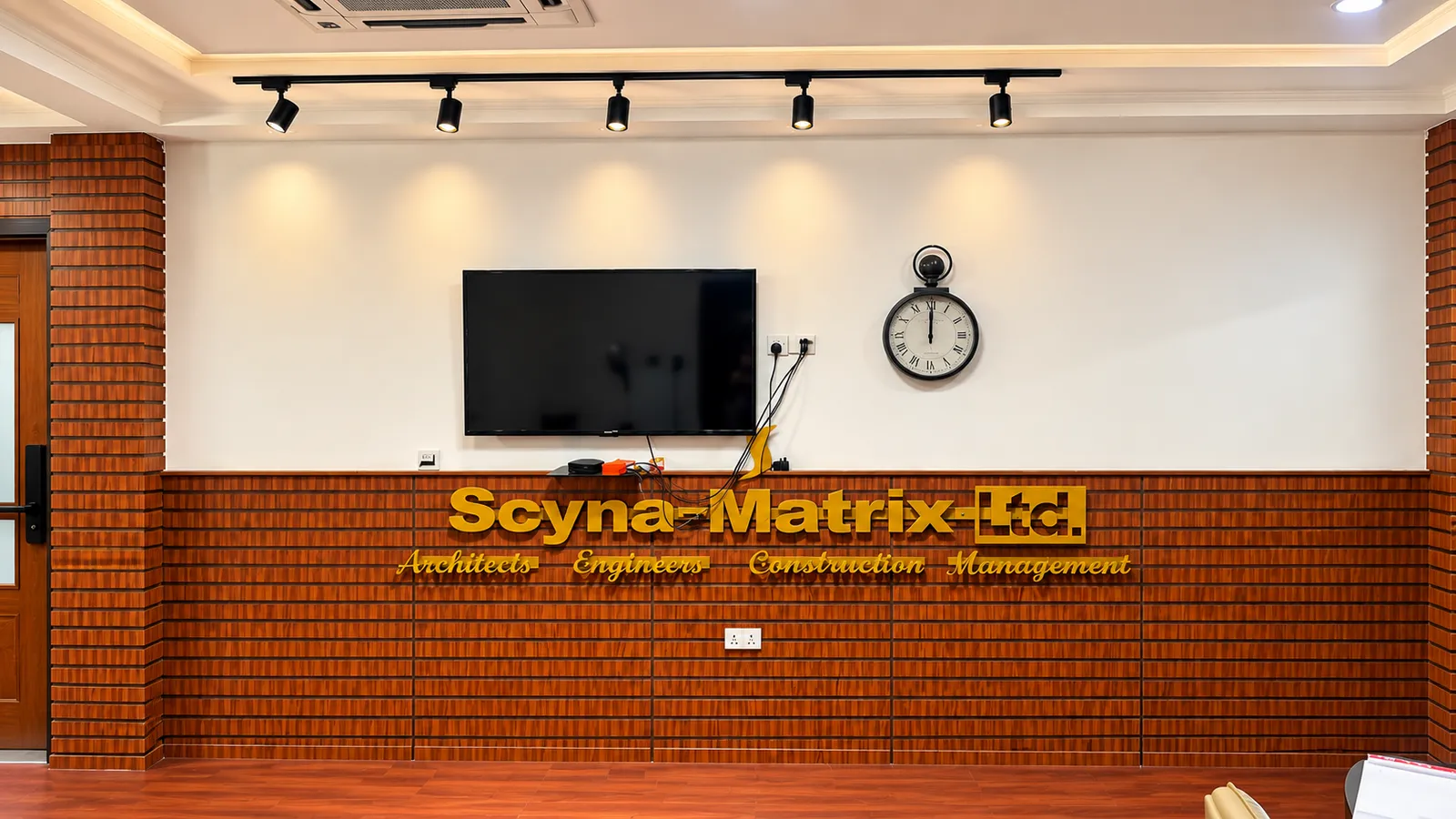 Office wall with gold lettering that reads Scyna-Matrix Ltd., Architects, Engineers, Construction Management.